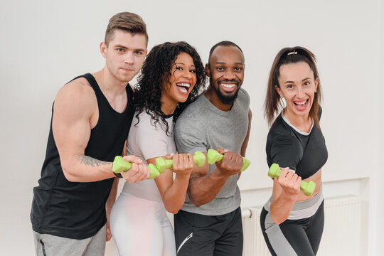 Group of young cheerful multinational people having fun and lifting weights in gym, Dynamic portrait featuring a happy and sporty multinational team, proudly holding dumbbells in a gym setting