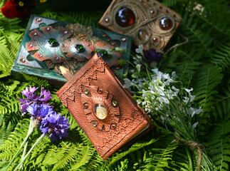Still life with beautiful magic book of spells or diary with flowers against green leaves. Occult,...