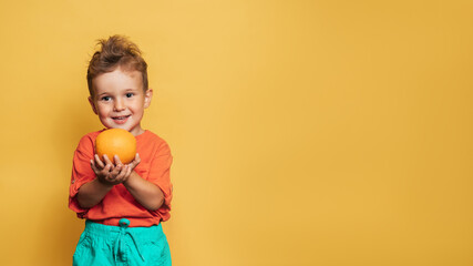 Studio shot of a smiling boy holding a fresh lemon and orange on a yellow background. The concept of healthy baby food, vitamin C. A place for your text.