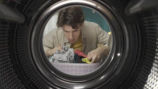 View from inside the washing machine, young man with laundry basket holds two different socks, searching for pair HDR BT2020 HLG Material.