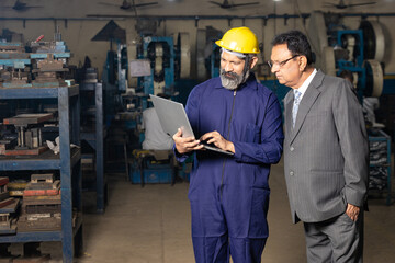 worker using laptop while discussing with factory owner