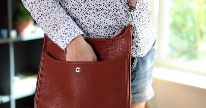 Woman puts smartphone in brown leather bag. Mobile data security in your phone