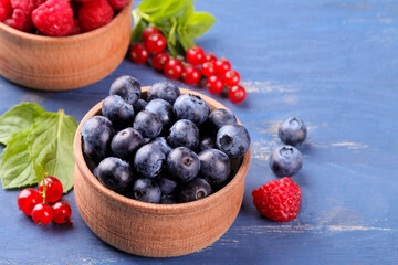 Blueberries in a bowl close-up and other berries, currants and raspberries in the background on a blue background