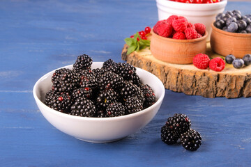 Blackberries in a bowl close-up and other berries, blueberries on a blue background.
