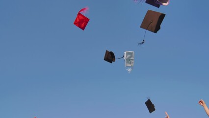 Graduates tossing multicolored hats against a blue sky.