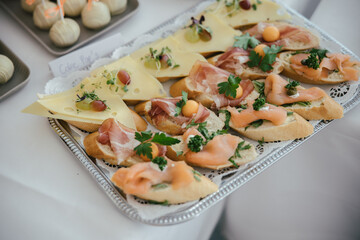 Delicious appetizers, baguette slices with cheese, cold cuts, and salmon on a silver tray at a buffet
