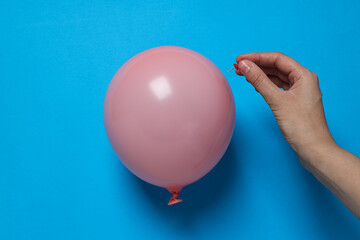 Balloon and hand with stationery needle on blue background