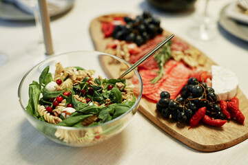 Appetizing homemade starter with green basil leaves and fusilli in glass bowl standing on served table next to fresh grapes and other snack
