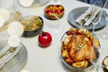 Appetizing roasted poultry with fried potatoes around and aromatic herbs on top standing on served table among flutes, plates and snacks