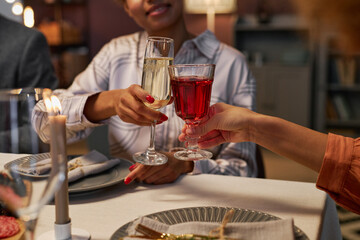 Hands of two young women clinking with flute of fizzy champagne and glass of red wine over table...