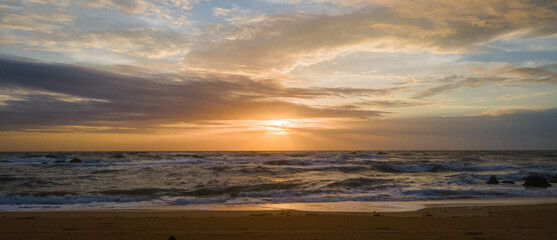 Sunset over ocean waves wash sand beach panorama