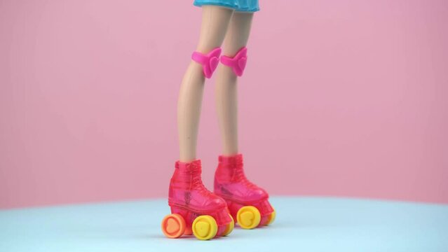 long slender legs of a barbie doll in roller skates and knee protection. rotation on pink and blue background. the concept of sports and recreation.