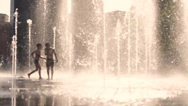 Children splashing in a city fountains on a hot summer evening. Unfocused or blurred view background, slow motion, 4K footage