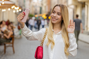 Blonde young woman blogger taking selfie on smartphone, communicating video call online with...