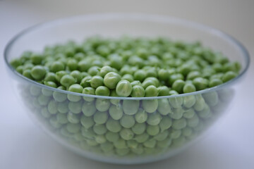 Green peas. Fresh peas in a clear glass bowl. Peeled sweet peas - obrazy, fototapety, plakaty