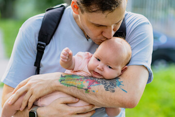 A dad with a tattoo cradles a newborn baby while standing on the street.
