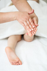 Doctor or a nurse massages the legs of a small child with her hands. Close-up of baby's foot