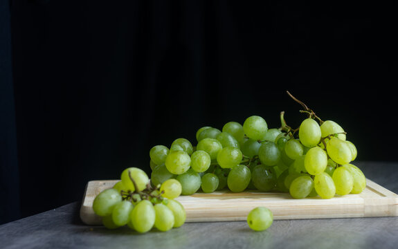 Bunches of green ripe grapes on a wooden board. On a dark background. Still Life high definition photography.