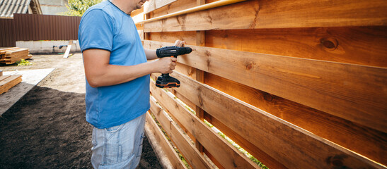 Adult man assembling a modern  wooden fence