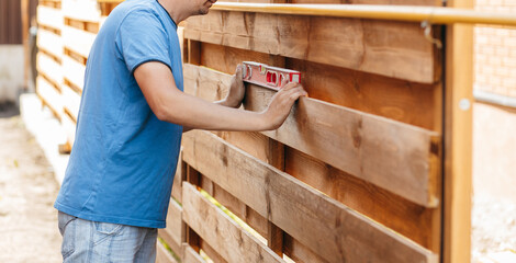 Adult man assembling a modern  wooden fence