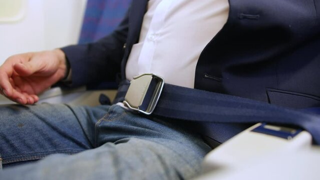 Close up of a man buckling and fastening seat belt on a passenger plane airliner airplane seat