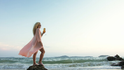 Attractive woman stand on a reef rock stone in sea on golden sunset. Girl on tropical beach in...