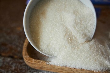 Sugar spilled from a bowl . Sweet substance for baking or ingestion