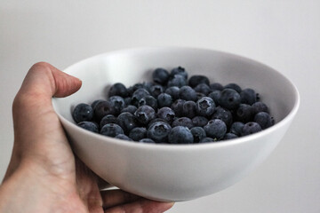 Hand holds a bowl of blueberry on white background.
White cup of fresh berries in the hand. Close up
