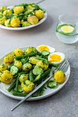 Delicious lunch or dinner, boiled young potatoes with asparagus beans and young fresh cucumbers, boiled eggs and fresh berries, refreshing water with lemon and mint