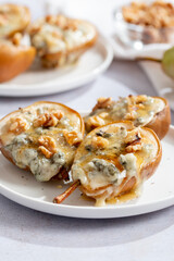 Baked pears with blue cheese, walnuts and honey on white plate and light background