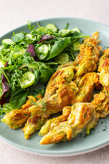 Fried zucchini flowers in batter and mix salad with cucumbers close up