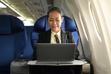 Middle age businesswoman using laptop in seat of a passenger on the board of plane