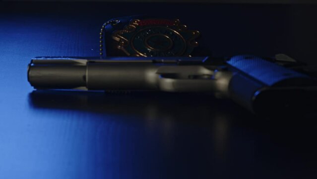 Wide pan over pistol lying on dark surface with a police badge and flashing lights in the background