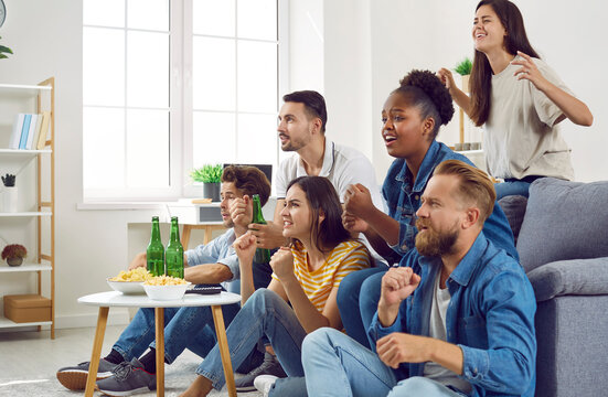 Group of friends sitting on sofa watching sport match together. Emotional male and female sports fans watching game together and supporting their team at home. Friendship, entertainment concept