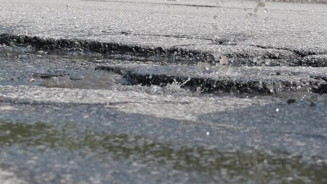 Car rides through potholes with water on bad asphalt road. Closeup
