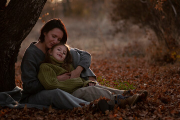 Mom and daughter in the autumn park are sitting under a tree.Yellow red leaves.Tender hugs close-up.
