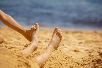 Child, tickling sibling on the beach on the feet with feather, kid cover in sand, smiling, laughing