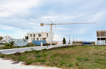 Fototapeta na wymiar Villa under construction. Tower crane on construction site. Prefabricated home сonstruction at Mediterranean sea. Construction of modern house on coastline in Spain. Home renovation. Build new home.