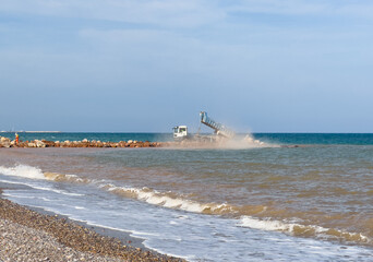 Breakwater construction at coastal. Beach regeneration on sea coastline. Dump truck unloads stones, Rubble during breakwater construction. Resort beach renovation. Shore protection. Built stone wall.
