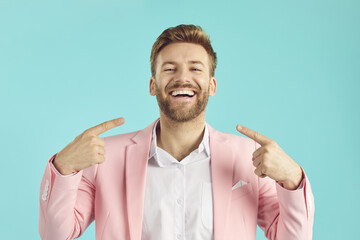 Happy, satisfied man in a pink suit and with a perfect smile points at his mouth, shows his even,...