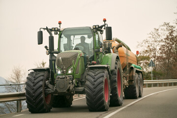 Agricultural Efforts in Motion. A Tractor at Work on a Sunny Summer Day. Farm tractor moving on the rural road near the farm © AlexGo