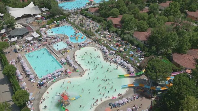 Drone orbits bird's eye view perspective above busy swimming pool with tourists