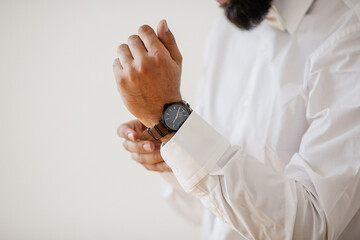 a man in a white shirt (groom) puts a black watch on his hand