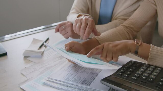 Cropped shot of hands of female financial advisor holding bills and using calculator while helping elderly woman with estimating expenses and planning budget