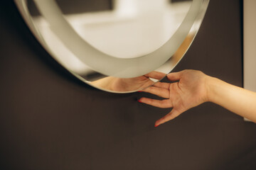 Woman's hand turns off the backlight of the bathroom mirror by touching the touch button on and off. Modern technologies