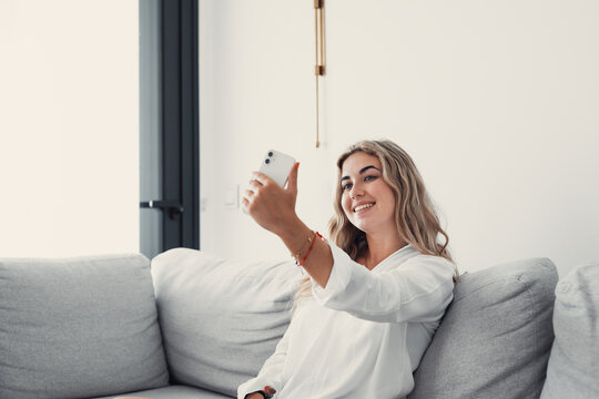 Selfie picture of happy beautiful young woman looking at camera with toothy smile. Pretty girl holding gadget with webcam, making video call, self home portrait. Communication concept.
