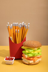hamburger and french fries from pencil, office supplies on color background, concept photo unhealthy office food