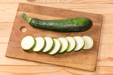 Whole and sliced dark green zucchini on the cutting board