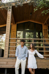 Trendy woman in sundress standing near brunette boyfriend and vacation house at background