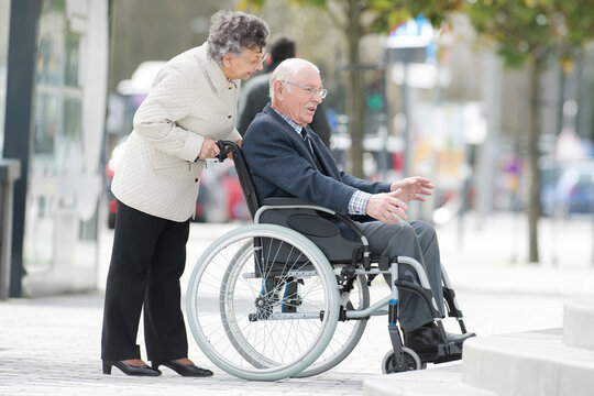 elderly lady in city pushing husband in wheelchair